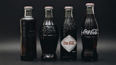 Four classic Coca-Cola glass bottles displayed on a dark, minimalist background for a vintage look.