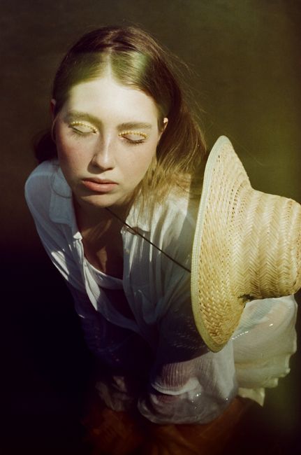 Artistic portrait of a young woman in a straw hat with eyes closed, evoking serenity.