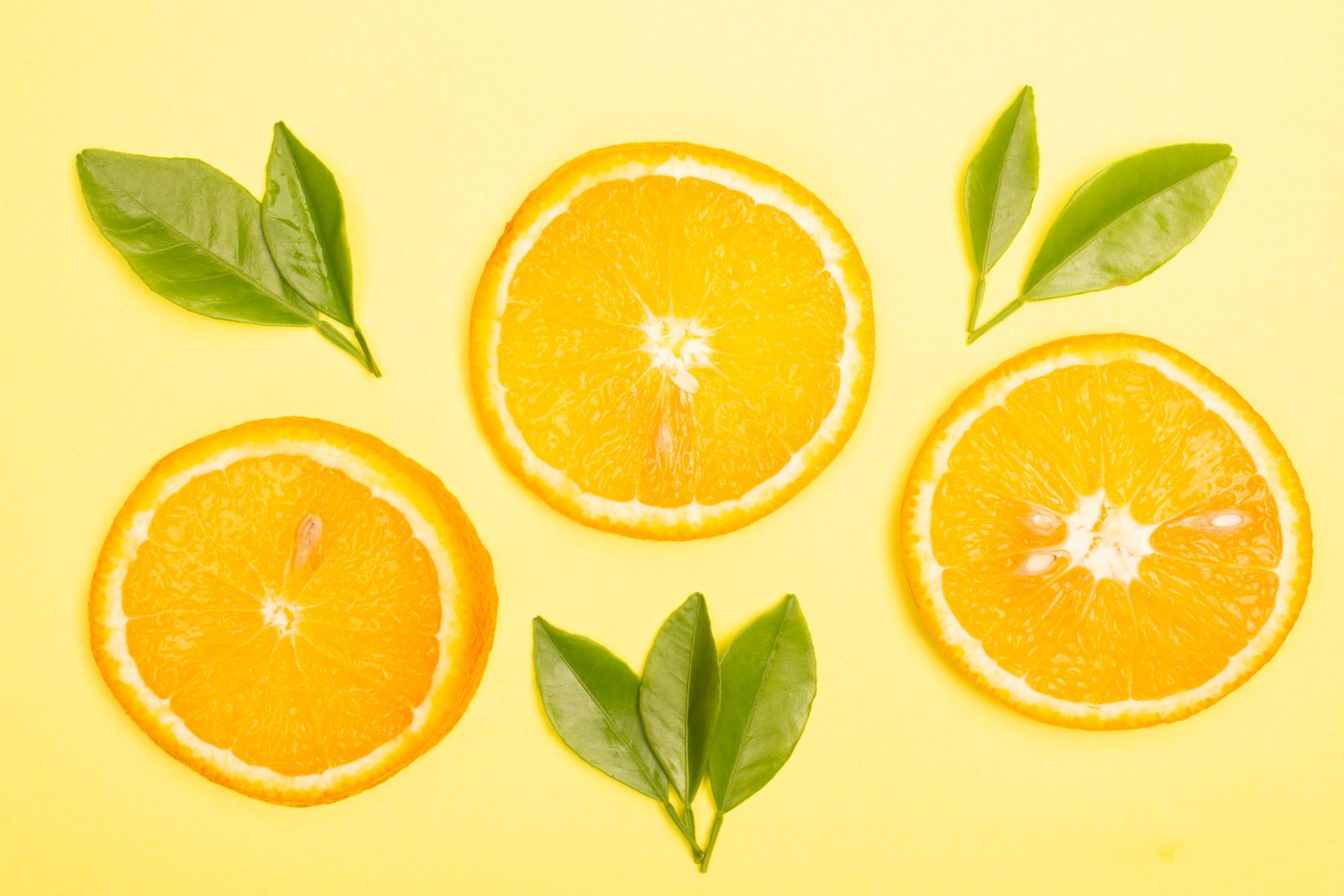 Vibrant orange slices and fresh green leaves arranged on a bright yellow background