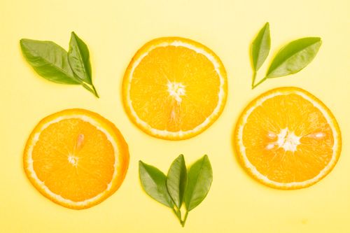 Free Bright orange slices and green leaves on a yellow background create a vivid citrus-themed flat lay. Stock Photo