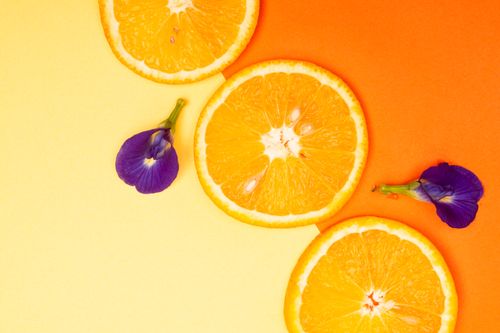 Free Vibrant orange slices with purple flowers on a yellow and orange background, offering a fresh, summery vibe. Stock Photo