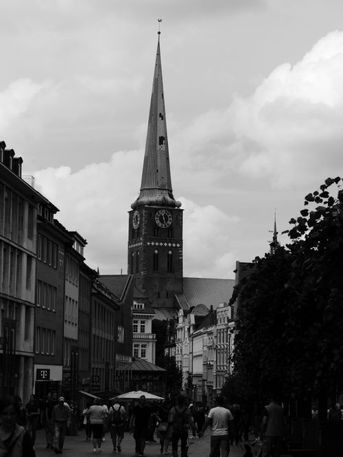 Free Black and white photo of a Gothic church tower with people in a bustling city street. Stock Photo