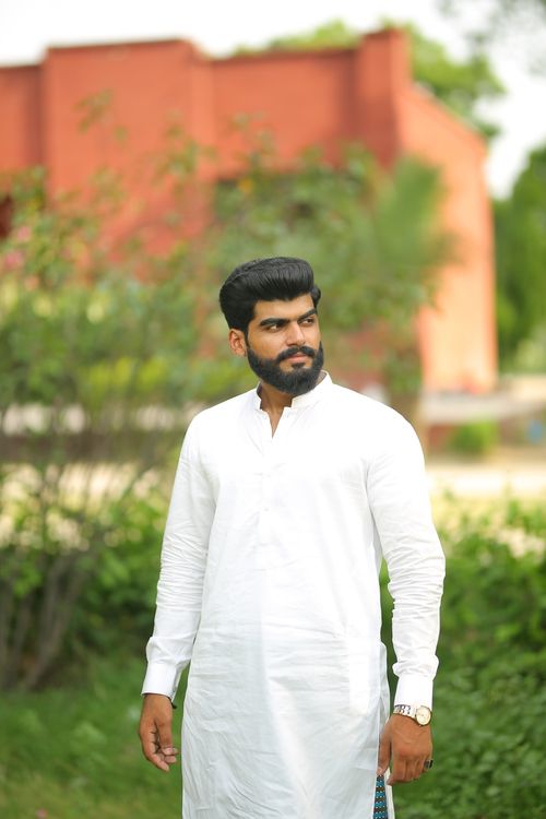 Free A man wearing a white thobe stands outdoors in a lush green setting in Lahore, Pakistan. Stock Photo