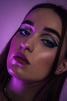 Close-up portrait of a woman featuring vibrant eye makeup and moody lighting.