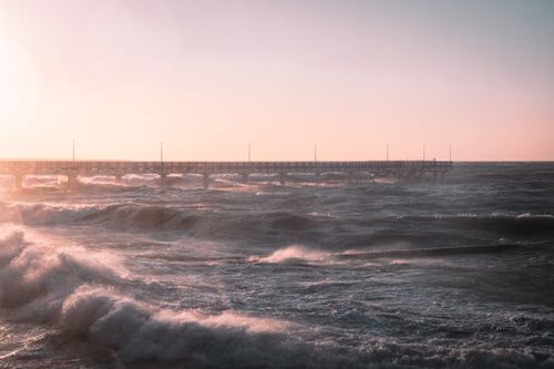 Free A breathtaking view of waves crashing against a pier at sunset, showcasing nature's power and beauty. Stock Photo