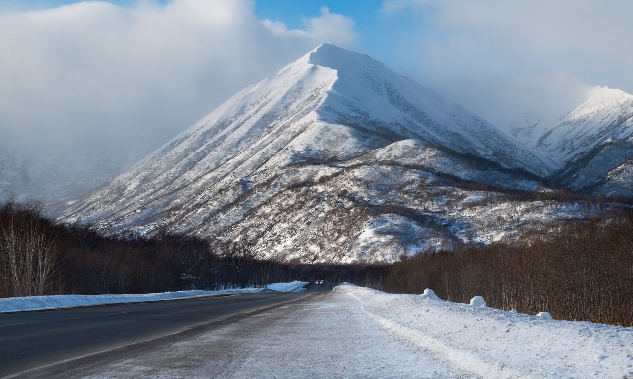 a scenic view of a snow covered mountain beside an icy road during win