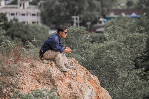 Man in Blue Long Sleeve Shirt Sitting on Brown Rock Formation