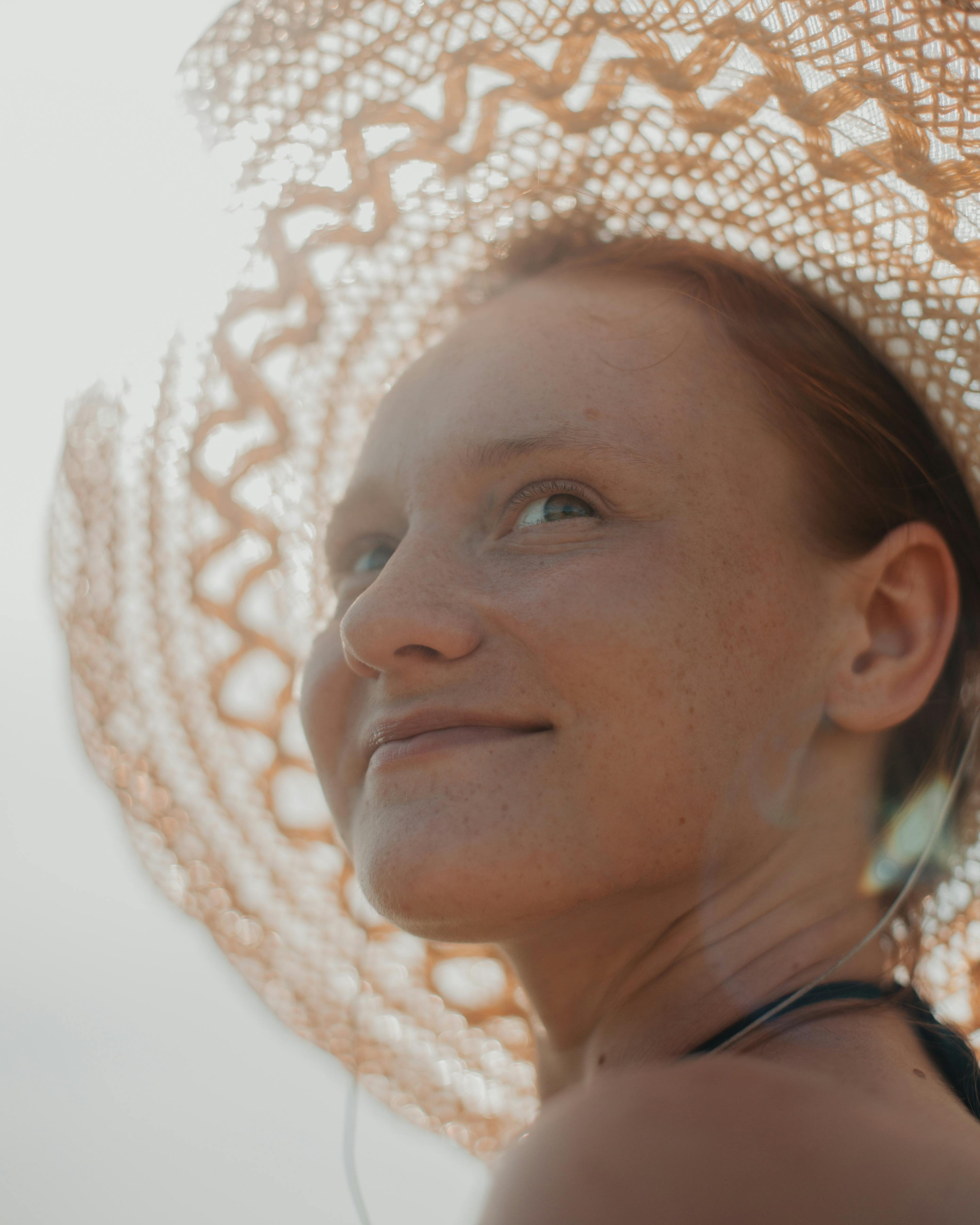 Close-up portrait of a smiling woman in a straw hat, capturing the essence of summer in a bright, warm setting.