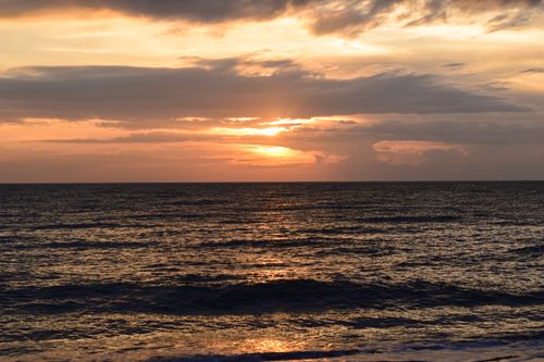 Free Peaceful sunset over ocean waves with vibrant orange sky and clouds. Stock Photo
