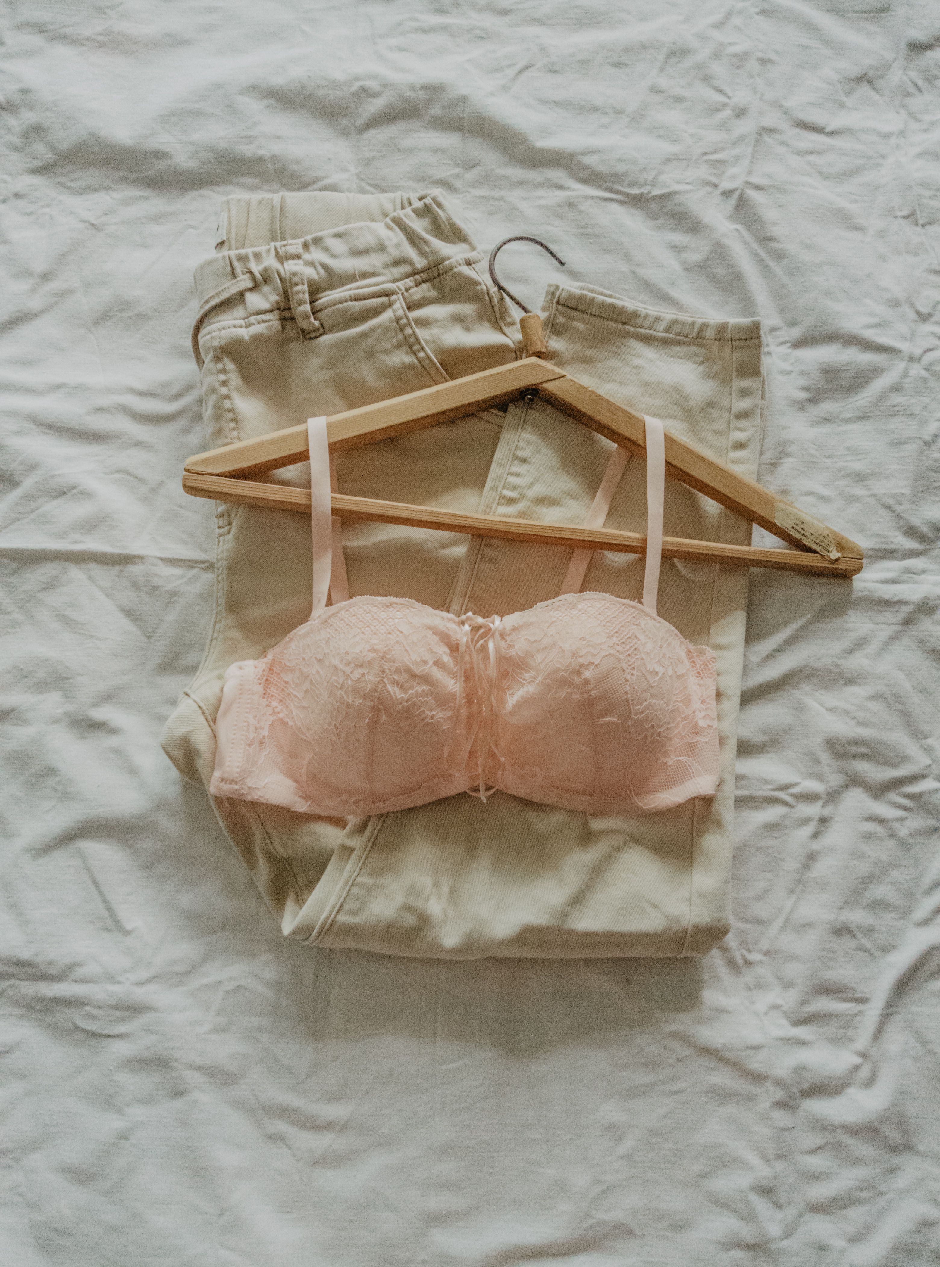 Beige pants and pink bra on a wooden hanger over white linen fabric.