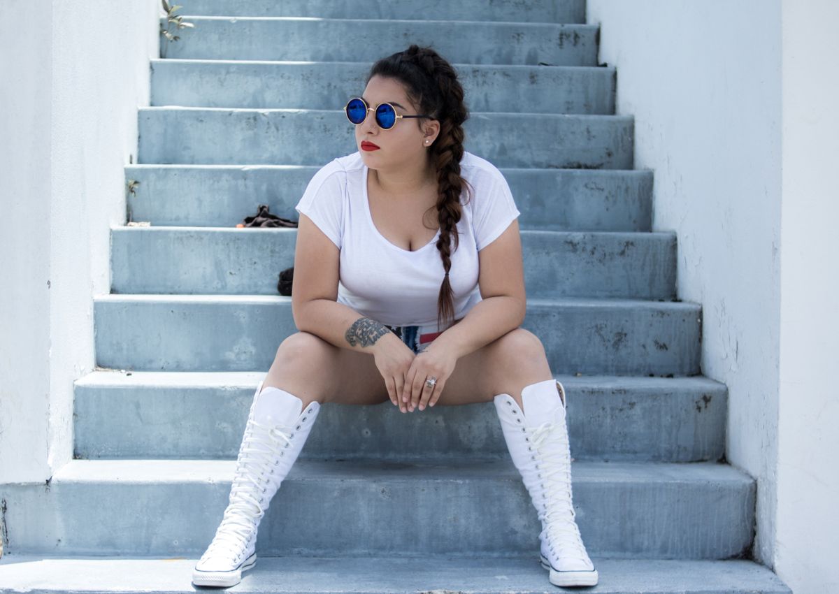 Fashionable woman styling white knee-high boots on a set of steps
