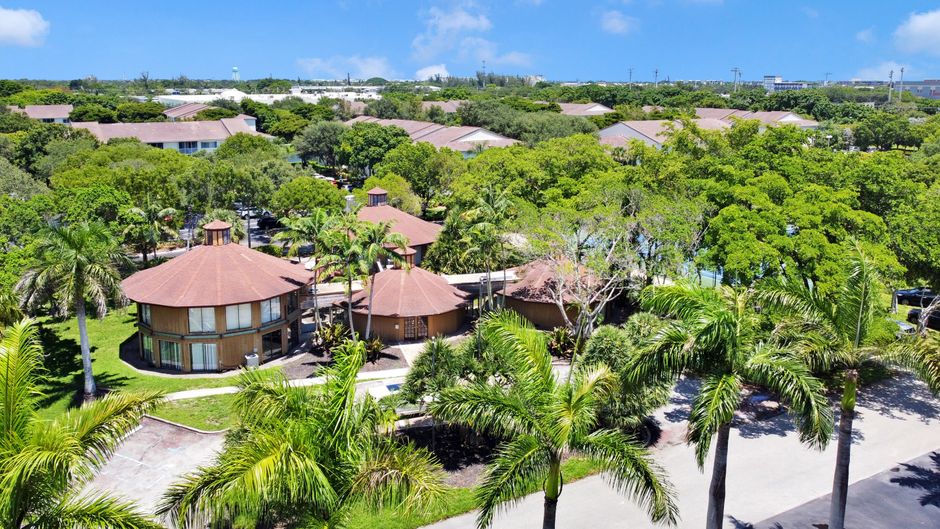 Photo by Barion McQueen Aerial view of a tropical resort with palm trees and round villas under a clear blue sky.