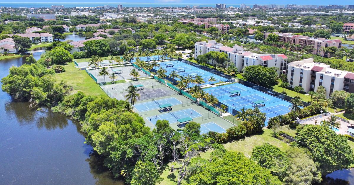 Aerial shot of tennis courts surrounded by lush greenery, apartments, and a river.