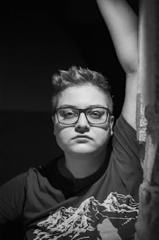 Monochrome portrait of a person with eyeglasses in a thoughtful pose.