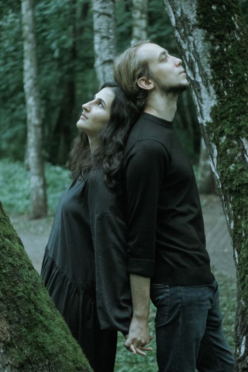 Free A couple stands back-to-back holding hands among tall trees in a serene forest. Stock Photo