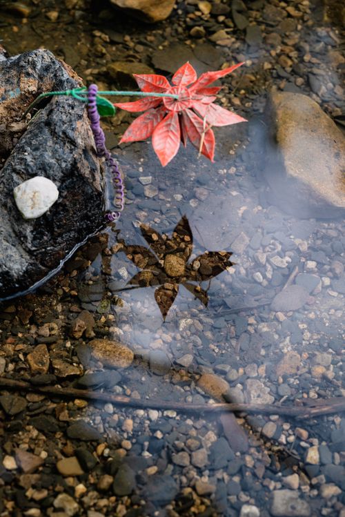 Free A striking red artificial flower with pebbles and rocks visible in clear water. Stock Photo