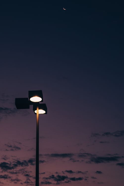 Free A silhouetted streetlight stands against the deep purple twilight sky with a crescent moon. Stock Photo