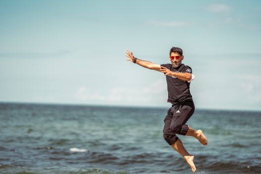 Energetic man jumps joyfully by the sea on a sunny day.