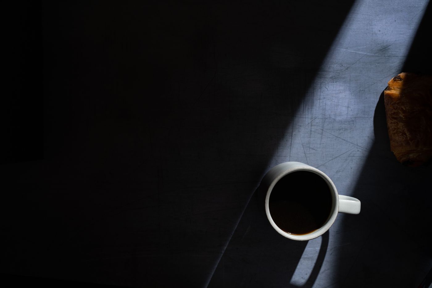 Moody image of a coffee cup and pastry with dramatic shadows in a flat lay composition.