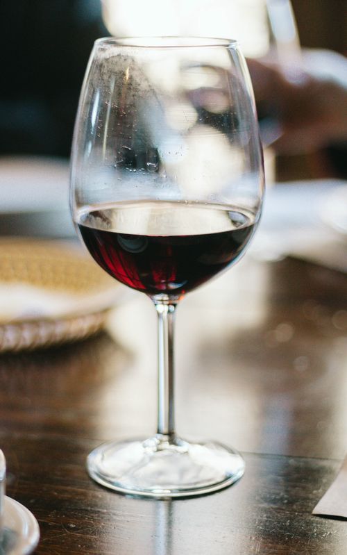 Free A close-up shot of a glass of red wine on a wooden table in a cozy indoor setting. Stock Photo