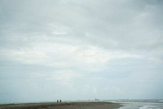Wide shot of a cloudy beach with two distant figures, offering ample copyspace.