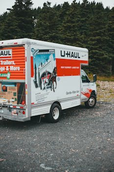 A U-Haul moving truck parked on gravel with trees in the background.