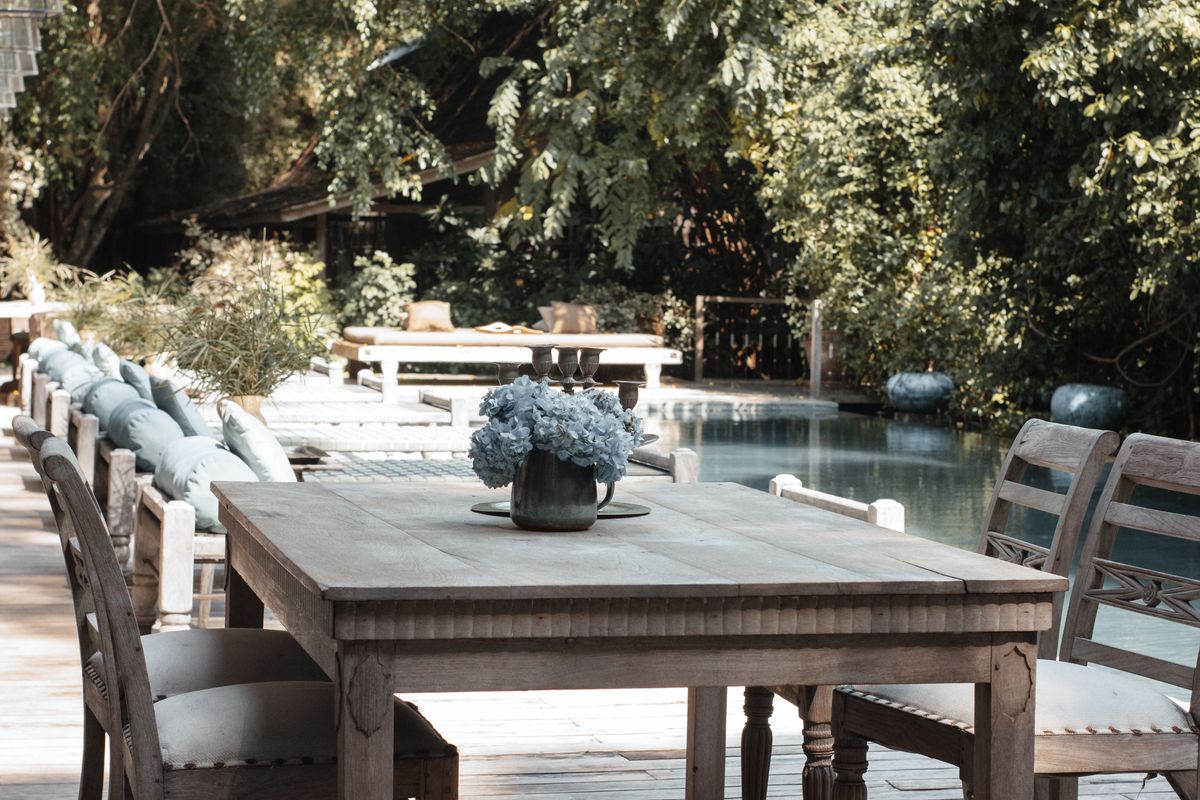 A serene outdoor dining area with wooden furniture and a flower vase by the poolside. Stock Photo.