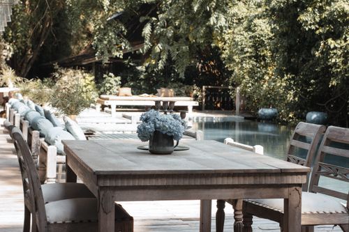 Free A serene outdoor dining area with wooden furniture and a flower vase by the poolside. Stock Photo
