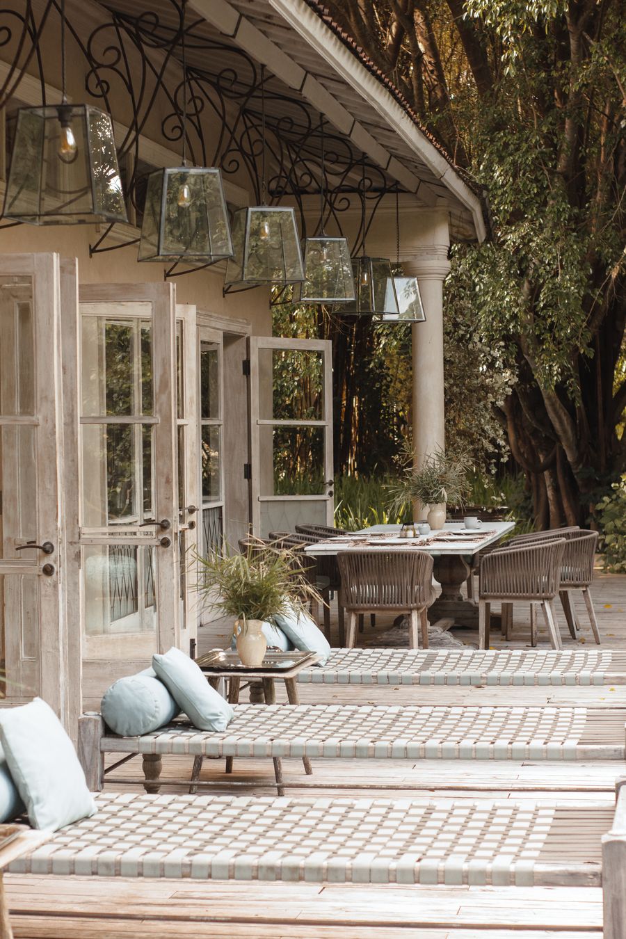 Outdoor lounge chairs and a dining table beneath a canopy of trees