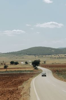 Long winding road through rural landscape with blue sky and mountains in the background.