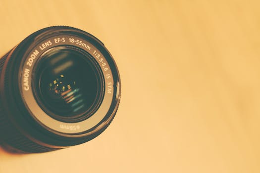 A detailed view of a camera lens with a reflection on a neutral backdrop.