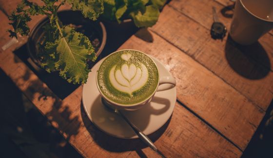 Green matcha latte with white tulip latte art in a cup on a rustic wooden table