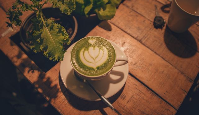A warm indoor scene of a matcha latte with beautiful latte art on a rustic wooden table.