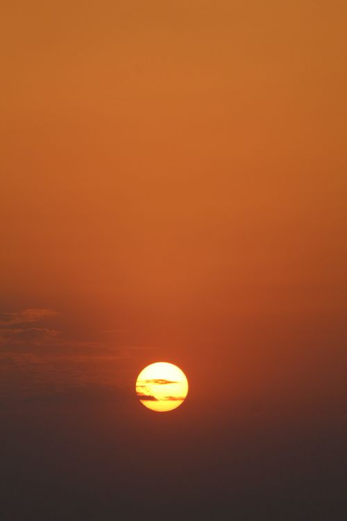 Free A tranquil sunset with a vivid orange sky and a visible sun on the horizon. Stock Photo