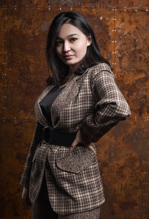 Free Confident woman in plaid blazer poses indoors with a rustic background. Stock Photo