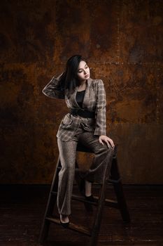 Woman in a plaid blazer and pants posing stylishly on a ladder in a studio setting.