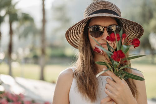Close-Up Shot of a Woman Wearing Sunglasses Holding Red Flowers