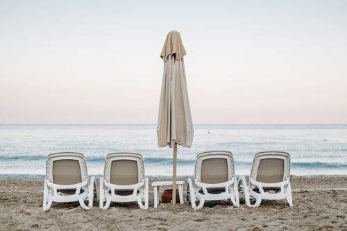 Free Empty lounge chairs and umbrella on a serene beach with ocean view. Stock Photo