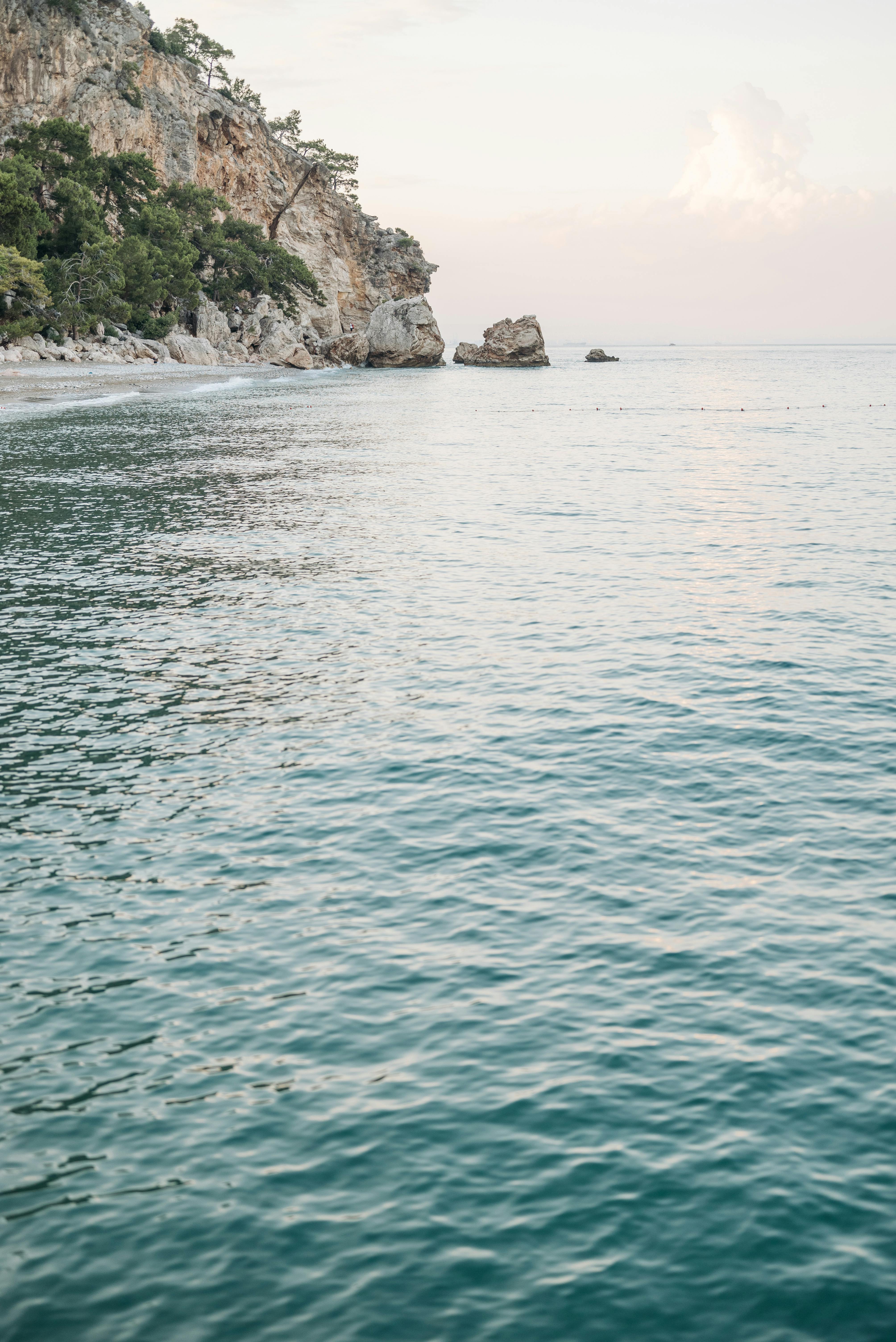 一个宁静的海滩场景，在柔和的天空下拥有平静的水域和岩石悬崖