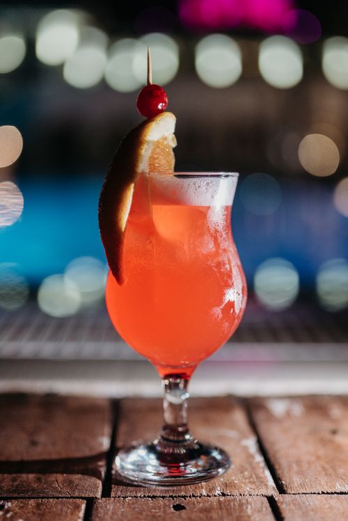 Free Close-up of a vibrant cocktail with orange and cherry garnish on wooden surface. Stock Photo