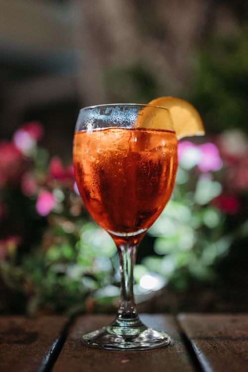 Free Close-up of a vibrant Aperol Spritz cocktail with an orange slice, outdoors, on a wooden table. Stock Photo