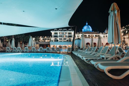A serene nighttime scene of a luxury hotel poolside with empty loungers and a beautifully lit dome.