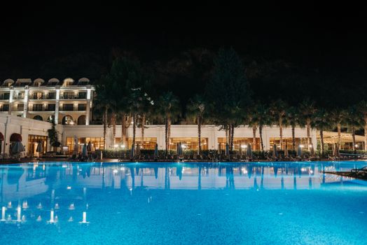Elegant nighttime view of a resort pool with palm trees and hotel lights.