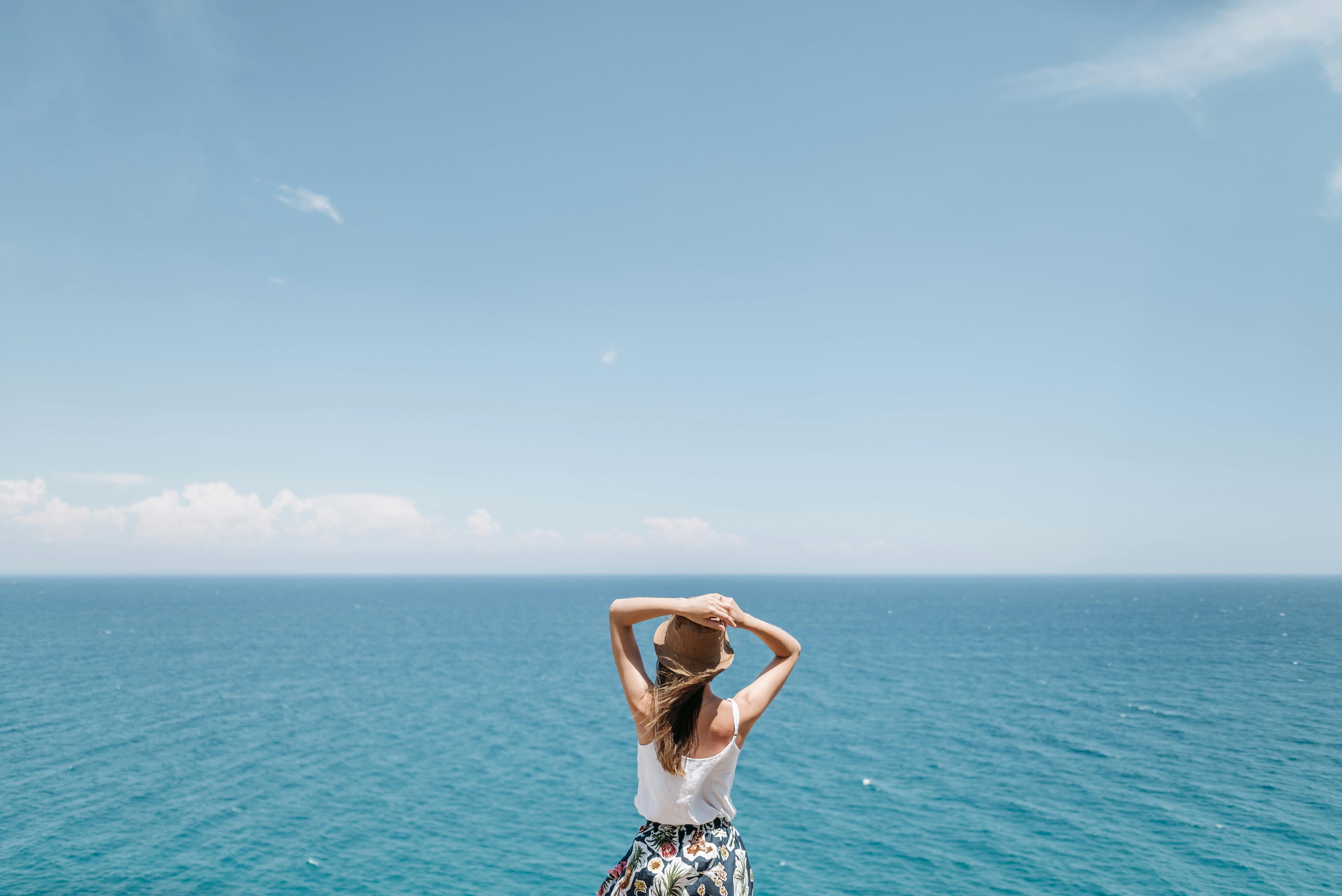 一个戴着夏季帽子的女人在阳光明媚的日子里欣赏着令人叹为观止的海景