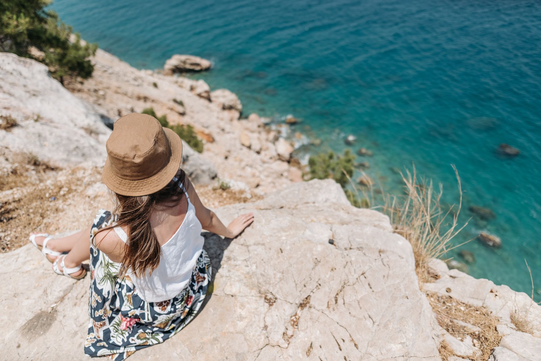 woman looking across a turquoise coastline from a cliff at sunset