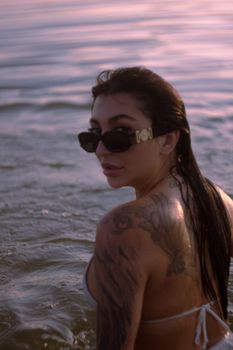 A woman with tattoos enjoys a swim while gazing back over her shoulder in stylish sunglasses.