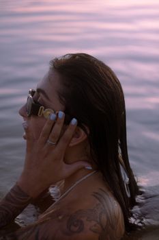 A tattooed woman with sunglasses enjoying a swim during sunset, showcasing a serene summer moment.