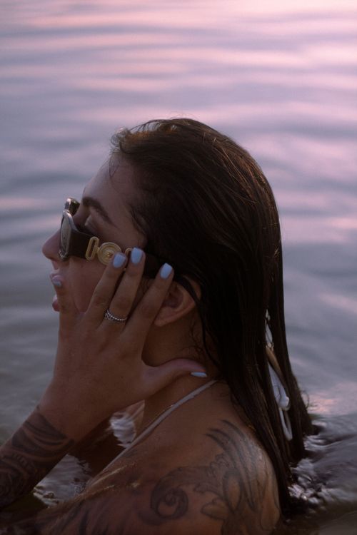 Free A tattooed woman with sunglasses enjoying a swim during sunset, showcasing a serene summer moment. Stock Photo