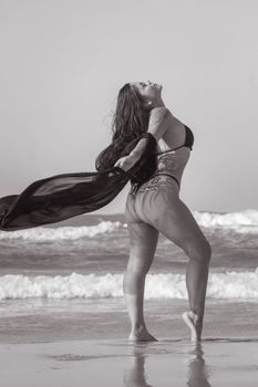 A woman stands gracefully on a Brazilian beach with a flowing scarf, embodying elegance and freedom.