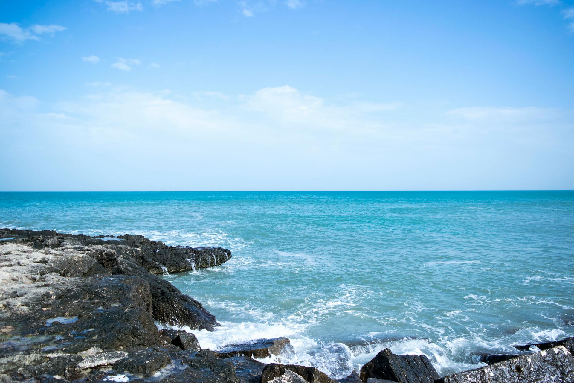 Serene ocean view with clear blue skies and rocky shoreline, perfect for nature themes.